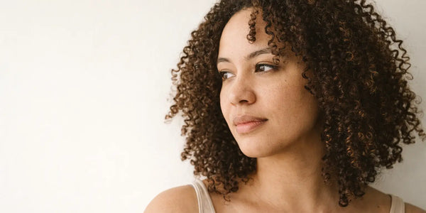 Soft daylight portrait of a woman with defined natural curls, representing healthy hair results associated with Keyoma.