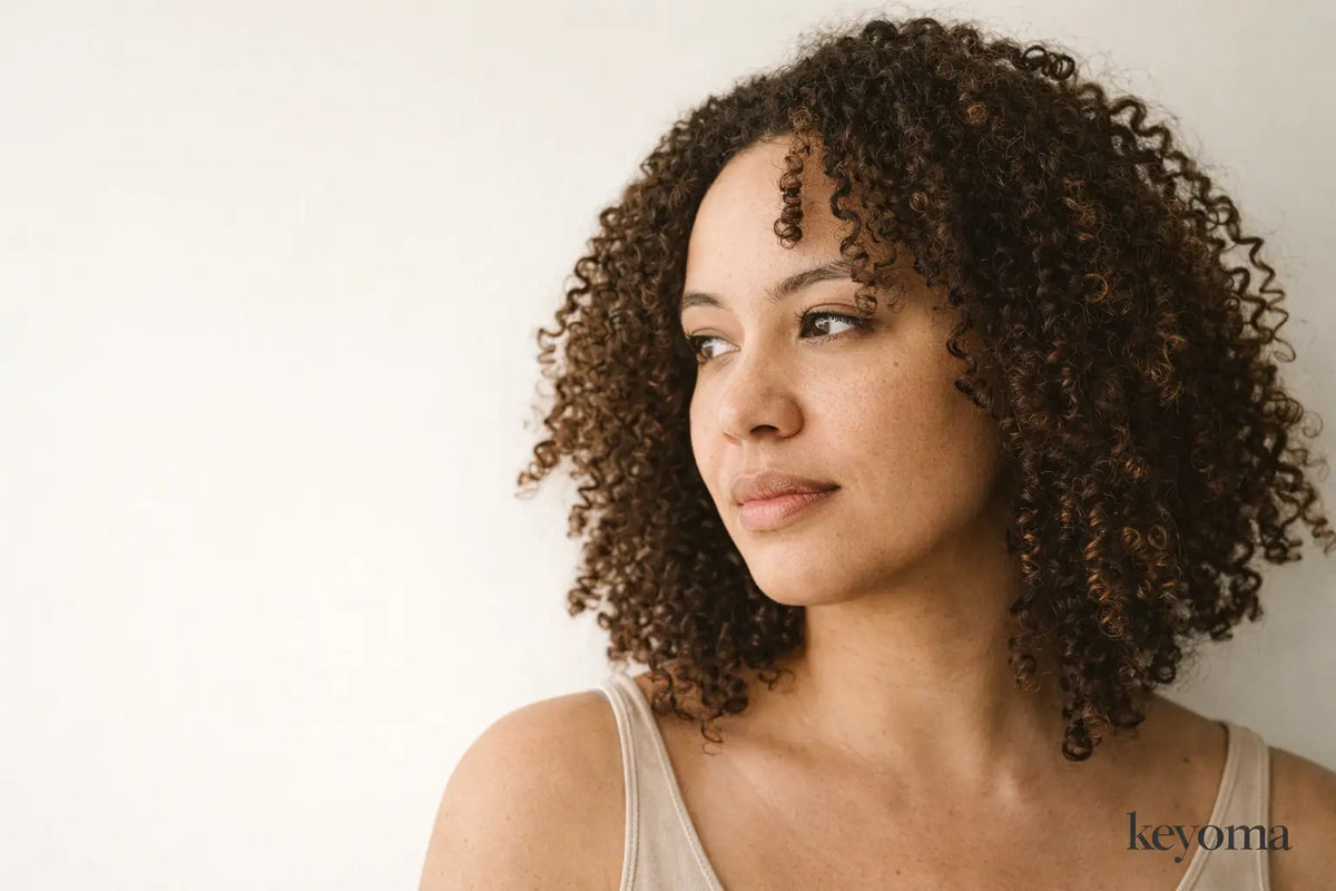 Soft daylight portrait of a woman with defined natural curls, representing healthy hair results associated with Keyoma.