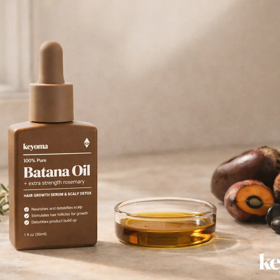 Closeup of Keyoma batana oil bottle on a vanity with oil bowl, nuts, and rosemary sprig.
