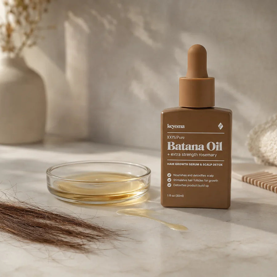 Keyoma Batana Oil bottle flatlay with loose hair strands, oil dish, comb, and towel.