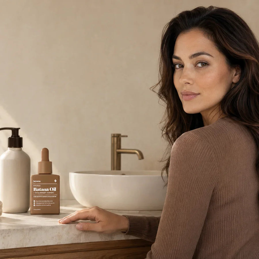 Keyoma batana oil bottle sits beside woman looking back at bathroom vanity.