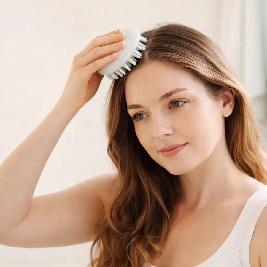 Woman gently uses a scalp brush during self care routine, illustrating Keyoma focused scalp stimulation benefits.